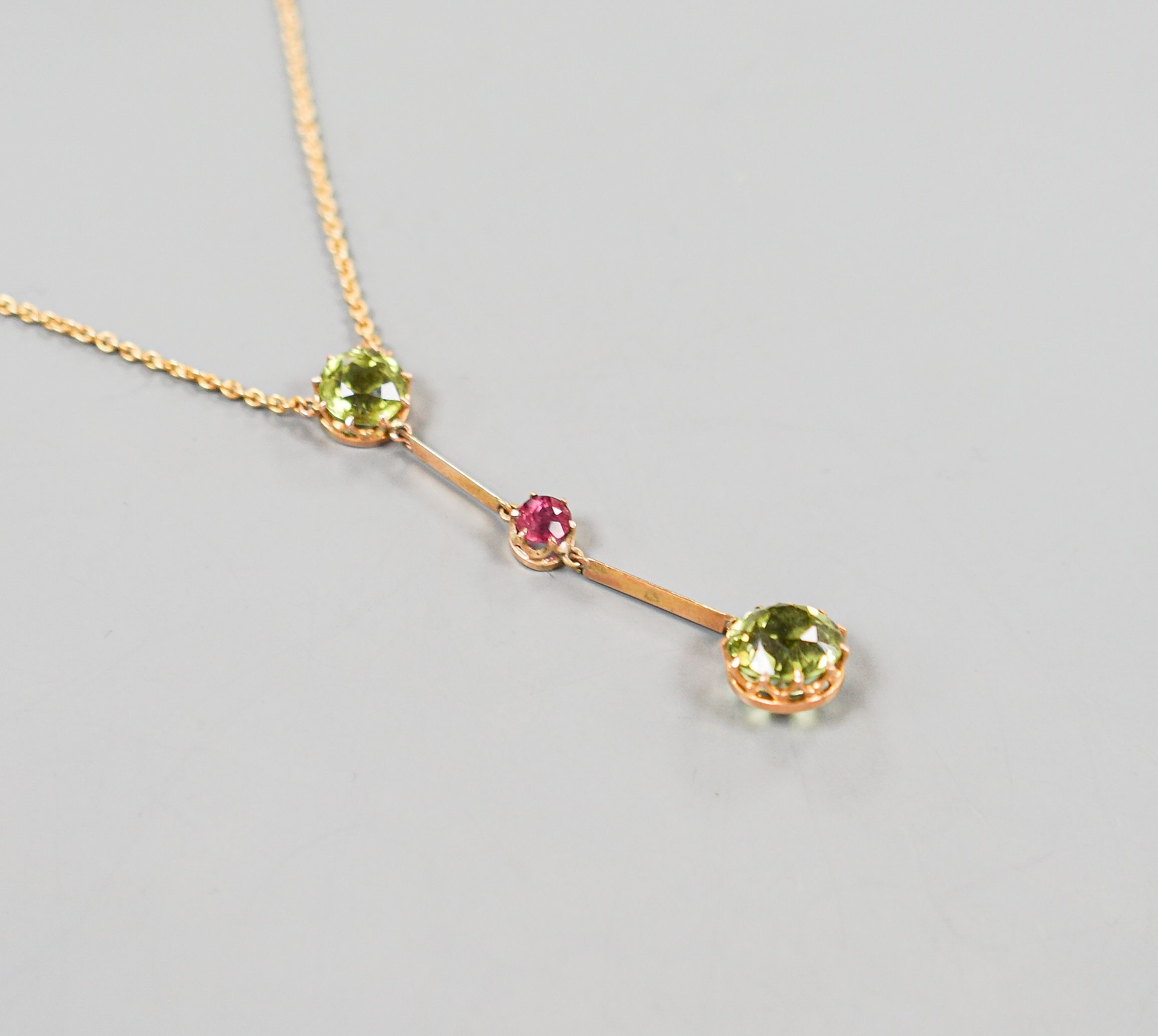 A 20th century yellow metal, two stone peridot and single stone pink tourmaline? set drop line pendant necklace, 51cm, gross 5.5 grams.